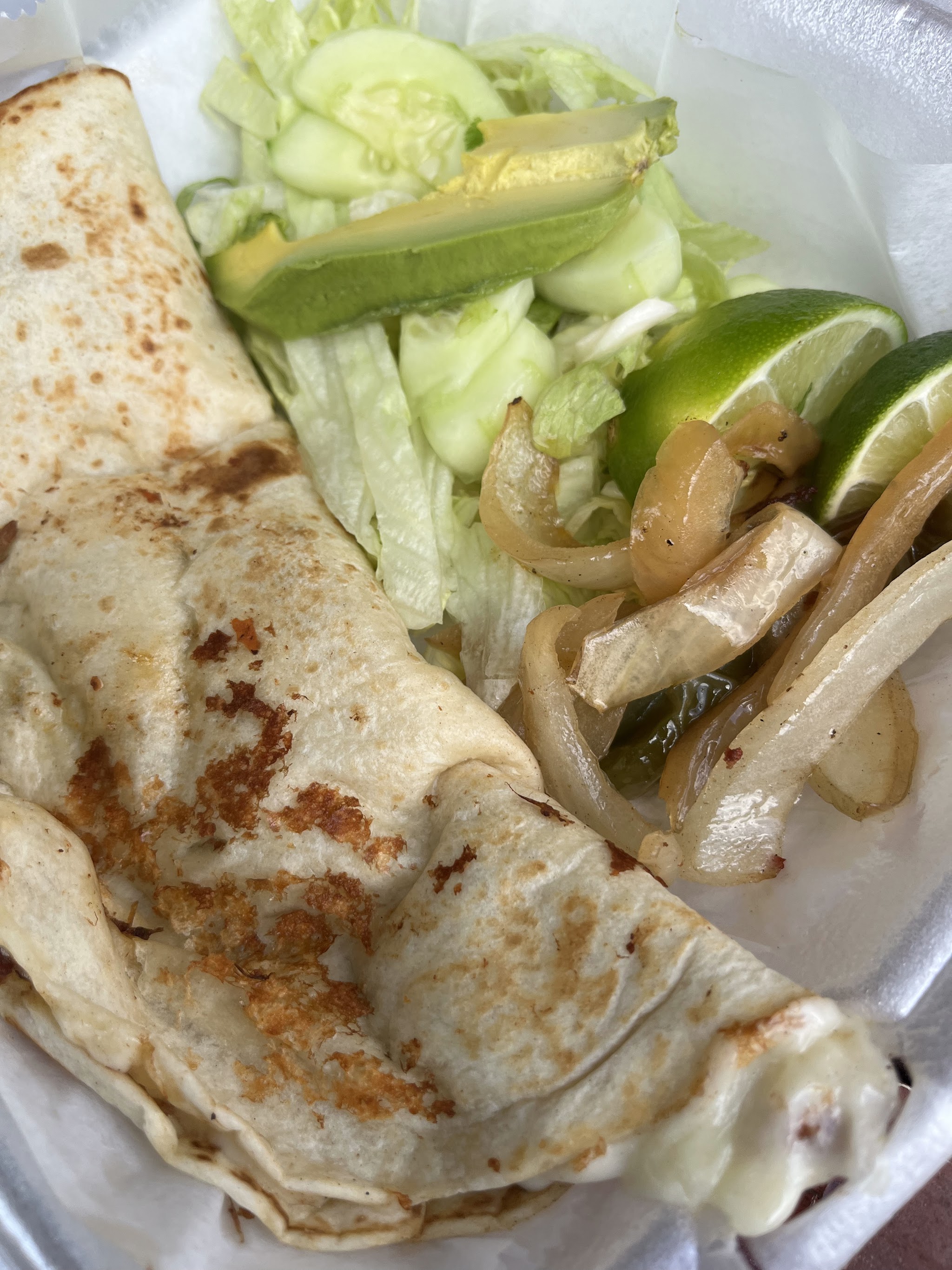 A folded quesadilla beside lettuce, cucumber, avocado and lime